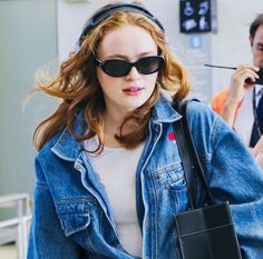 a woman wearing sunglasses and carrying a cell phone in her hand while walking through an airport