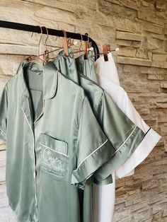 two shirts hanging on a clothes rack in front of a stone wall