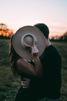 a man and woman embracing each other with a hat on their head in the middle of a field