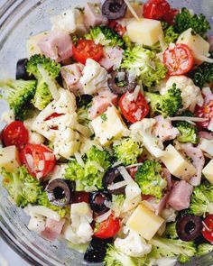 a salad with broccoli, tomatoes, olives and ham in a glass bowl