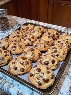 chocolate chip cookies sitting on top of a cookie sheet next to a jar of nuts