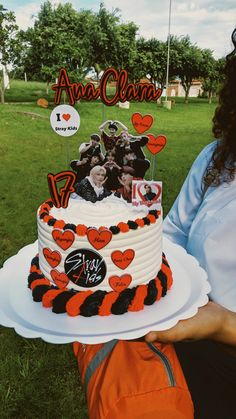 a woman holding up a cake with photos on it in front of an open field