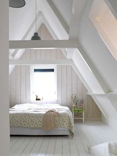 an attic bedroom with white painted walls and wood flooring, along with a bed in the center