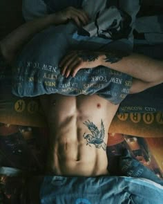 a shirtless man laying in bed with tattoos on his chest and arms above his head