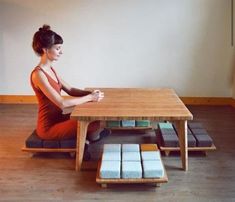 a woman sitting at a wooden table with mattresses on the bottom shelf and in front of her