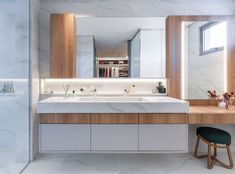 a modern bathroom with marble counter tops and wooden cabinets, along with two stools