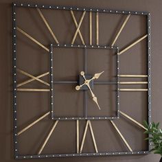 a square metal clock mounted to the wall next to a vase with a plant in it