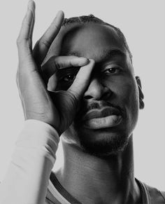 a black and white photo of a man holding his hand up to his face while looking at the camera