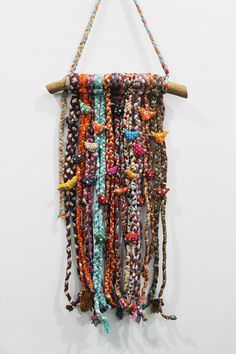 a multicolored beaded wall hanging on a white wall next to a wooden stick