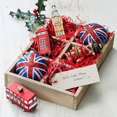 a wooden box filled with christmas ornaments on top of a white table next to a red truck