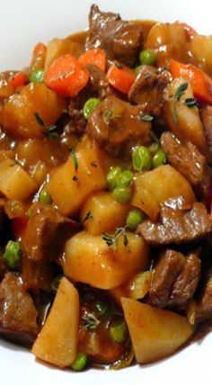 a white plate topped with beef and potatoes covered in sauce, garnished with fresh herbs