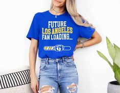 Get ready for game day with our comfy and stylish "Future Los Angeles Fan Loading" shirt. This football pregnancy announcement tee is the perfect way to share your exciting news with fellow LA fans. Made with soft, high-quality materials, it's ideal for game day, family gatherings, or casual wear. Mod Reveals is not affiliated with the NFL. Team Spirit Slogan Tops For Fans, Team Spirit Slogan Tops For Fan Gear, Game Day Fan Apparel T-shirt With Slogan, Game Day Sports Fan Slogan Tops, Sports Fan Slogan Tops For Game Day, Slogan Fan Gear Tops, Football Pregnancy Announcement, Digital Announcement, Growing Family