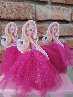 three barbie dolls in pink tutu skirts sitting on a table next to a brick wall