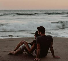 two people sitting on the beach watching the waves