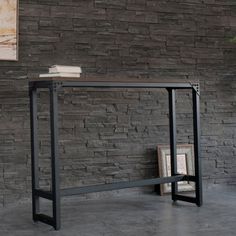 a book shelf sitting on top of a metal table next to a brick wall with a painting hanging above it