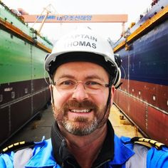 a man wearing a hard hat standing in front of large cargo containers at a shipyard