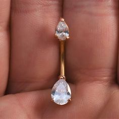 a close up of a person's hand holding a gold ring with two pear shaped diamonds