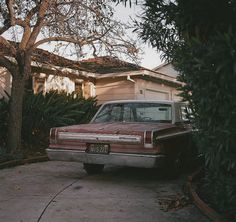 an old car parked in front of a house with trees and bushes around it's perimeter