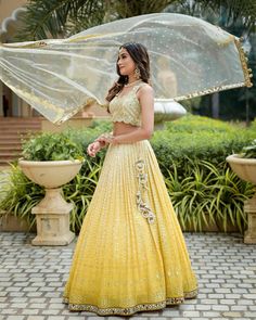 a woman wearing a yellow lehenga and matching with a white netted dupatta