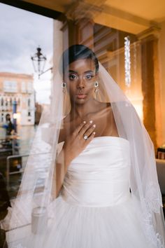 a woman wearing a wedding dress and holding a ring in front of a glass window