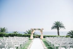 an outdoor ceremony setup with white chairs and flowers on the aisle, overlooking the ocean