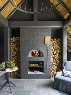 an outdoor fireplace with logs stacked in front of it and a couch next to it