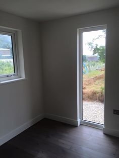 an empty room with two windows and a hard wood floor in front of the sliding glass door