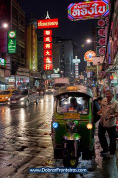 an auto rickshaw driving down a busy city street at night with neon signs in the background