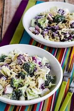 two white bowls filled with pasta and broccoli on top of a colorful table cloth