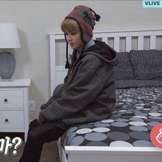 a young boy sitting on top of a bed next to a white dresser and night stand