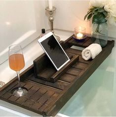 a bath tub with a tablet on top of it next to a glass of wine