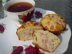 three muffins on a plate next to a cup of tea and rose petals