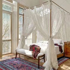 a canopy bed with sheer curtains and pillows on top of it, in a bedroom