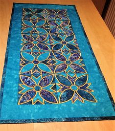 a table runner with blue and gold designs on it, sitting on top of a wooden table