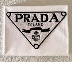 a white towel with the words prada in black and white on it, sitting next to a wall