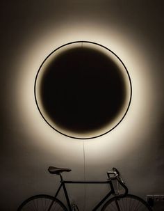 a bicycle is parked in front of a circular light that's on the wall