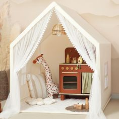 a doll house with a giraffe sitting in it's corner and pillows on the floor