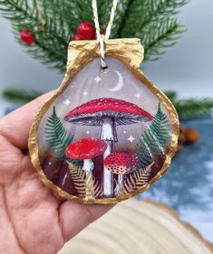 a hand holding a glass ornament with mushrooms and pine needles on it's side