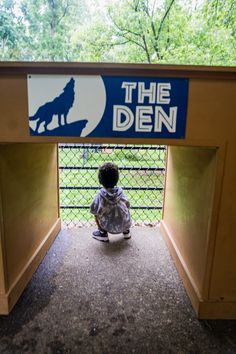 a small child is sitting on the ground in front of a sign that says the den