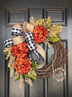 an orange and black wreath on the front door with plaid bow hanging from it's side