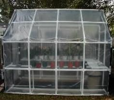 a large greenhouse with several plants inside of it on the grass in front of a house