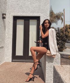 a woman sitting on the ledge of a building with her legs crossed and wearing high heels