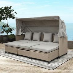 an outdoor daybed with four pillows and a cover over it on a deck overlooking the ocean