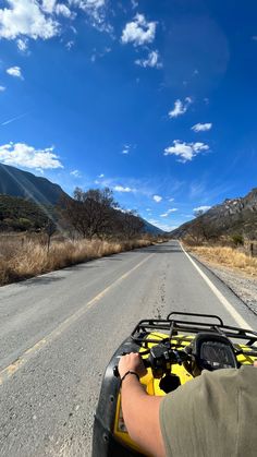 a person riding an atv down the middle of a road with mountains in the background