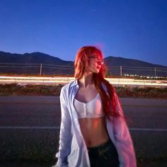 a woman with red hair and glasses standing in the middle of an empty road at night