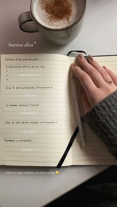 a person's hand on top of an open notebook next to a cup of coffee