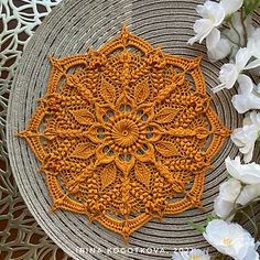 an orange crocheted doily sitting on top of a table next to white flowers