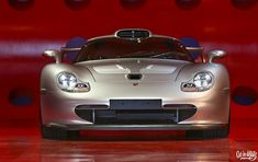 a silver sports car parked in front of a red wall