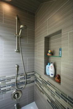 a bathroom with gray tile and white fixtures, including a shower head and hand held faucet