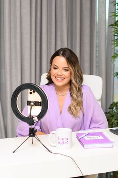 a woman sitting at a desk with a camera and coffee mug in front of her